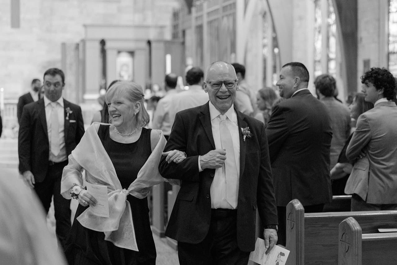 Tony and Mrs. Case walking down a church aisle smiling at Justin and Claire’s wedding